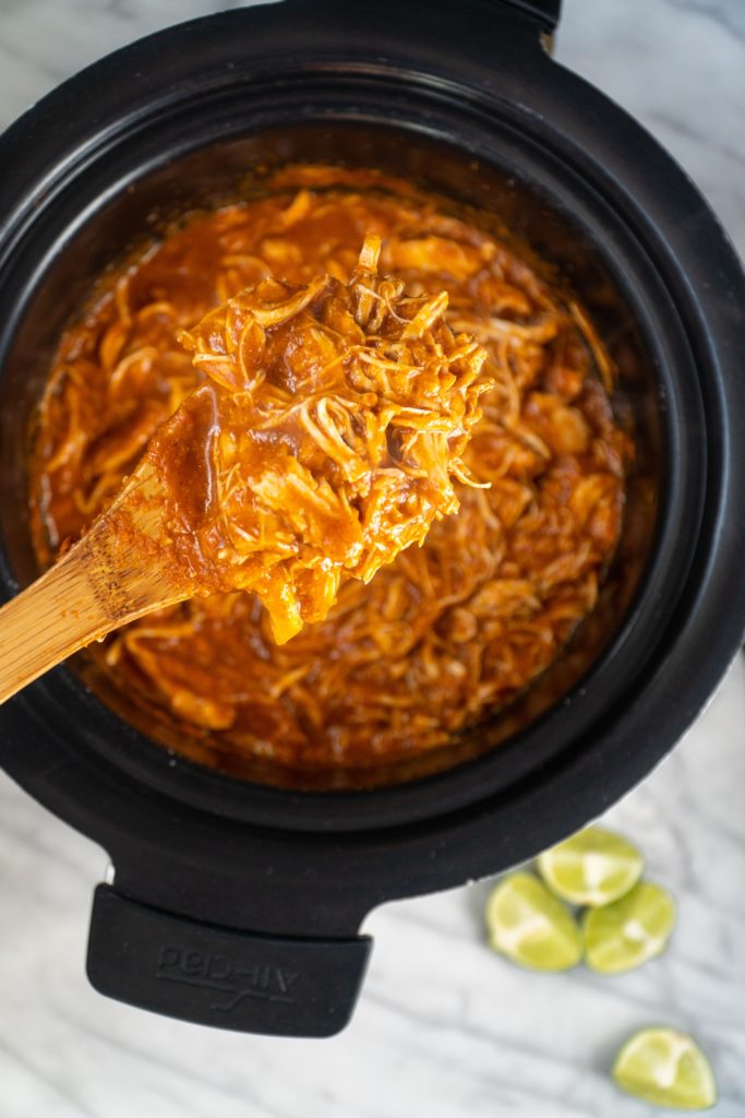 Slow Cooker Chicken Tinga in slow cooker with spoon and limes on the side