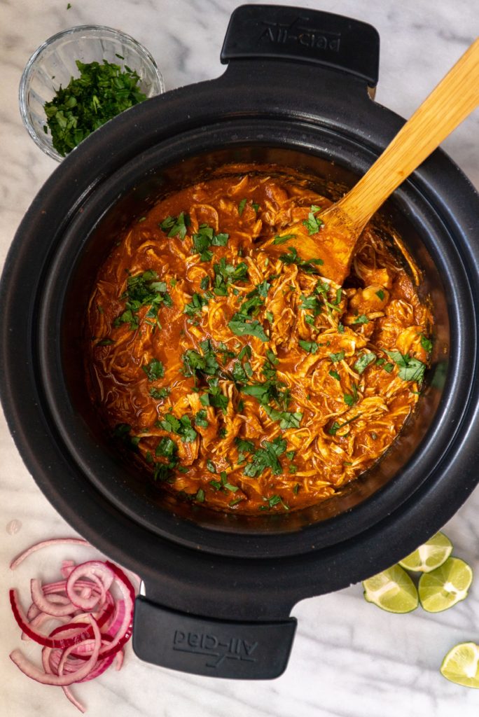 Slow Cooker Chicken Tinga sprinkled with cilantro in Slow Cooker with limes and onion on the side