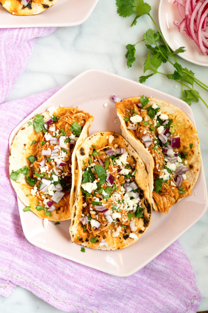 Chicken Tinga Tacos sprinkled with cilantro, goat cheese, and red onion 