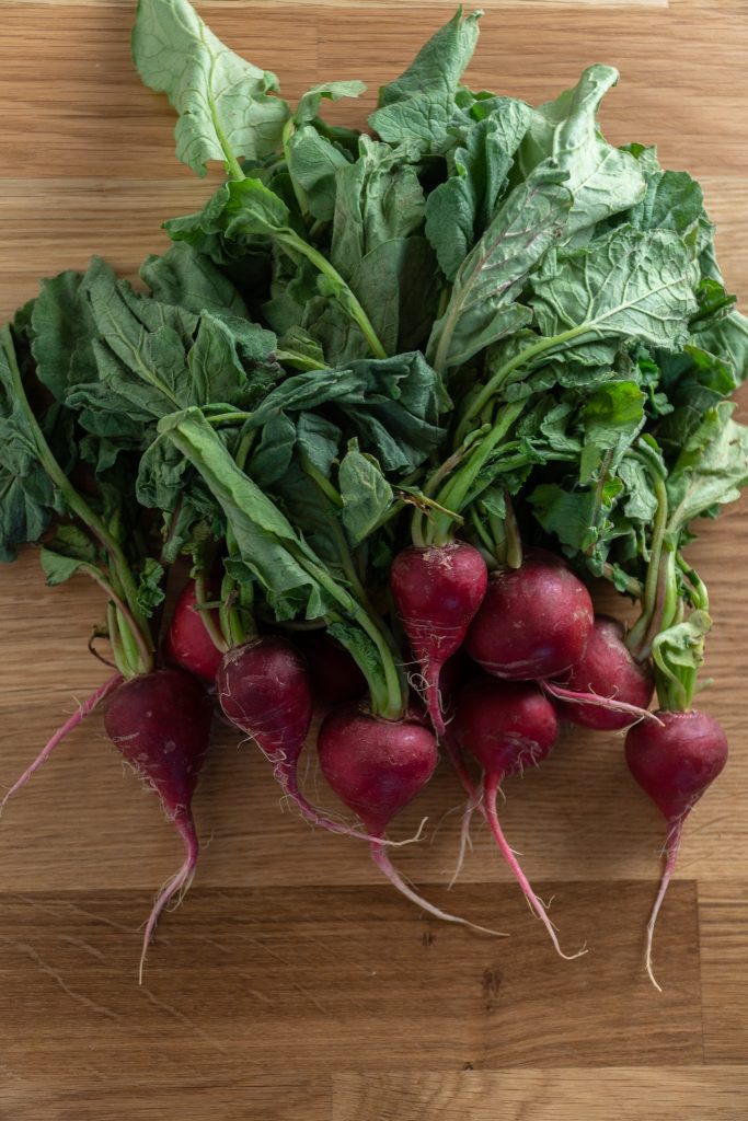 A bunch of radishes with leafy greens on a wooden cutting board