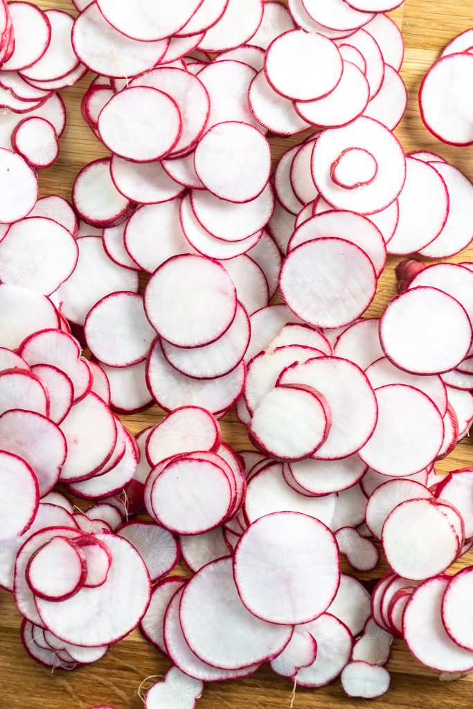 Thinly sliced radishes on a wooden cutting board