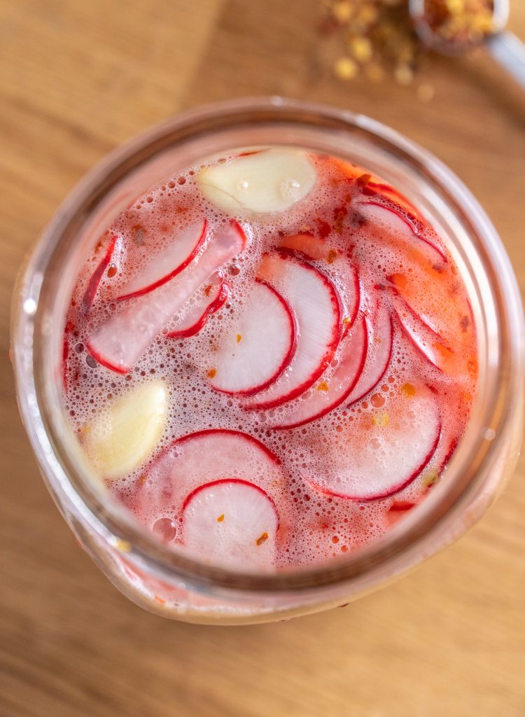 Looking down into a jar of thinly sliced quick pickled radishes with garlic cloves